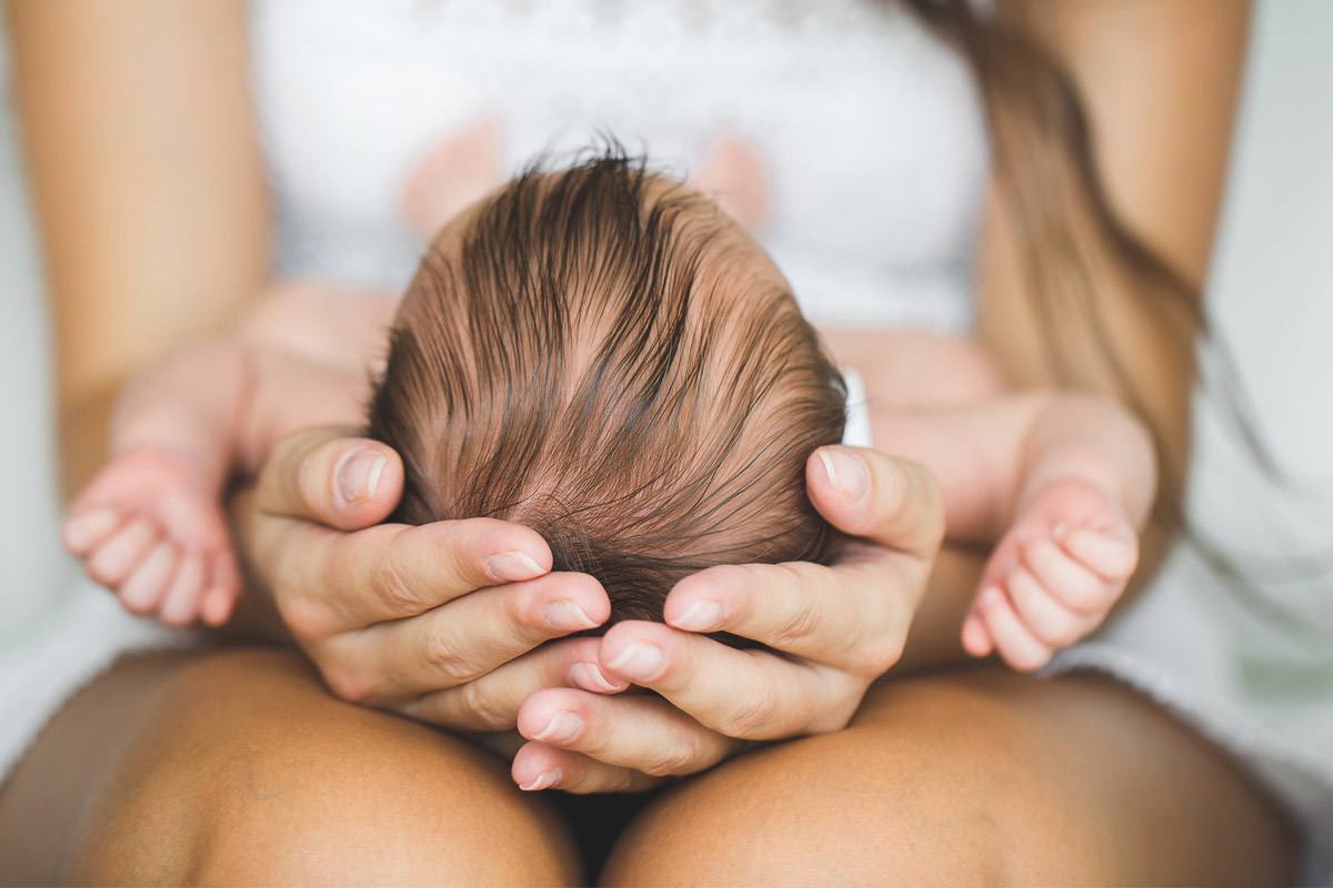 Mamma che tiene tra le mani la testolina del suo bambino - come prevenire la plagiocefalia