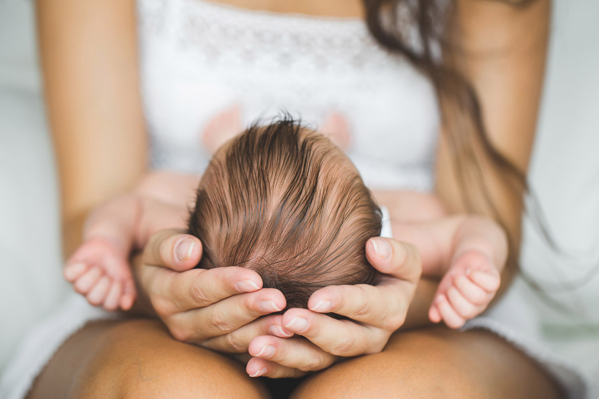 Le cure primarie del neonato - mamma che tiene tra le mani la testolina del suo bambino - come prendersi cura del cuoi capelluto dei neonati