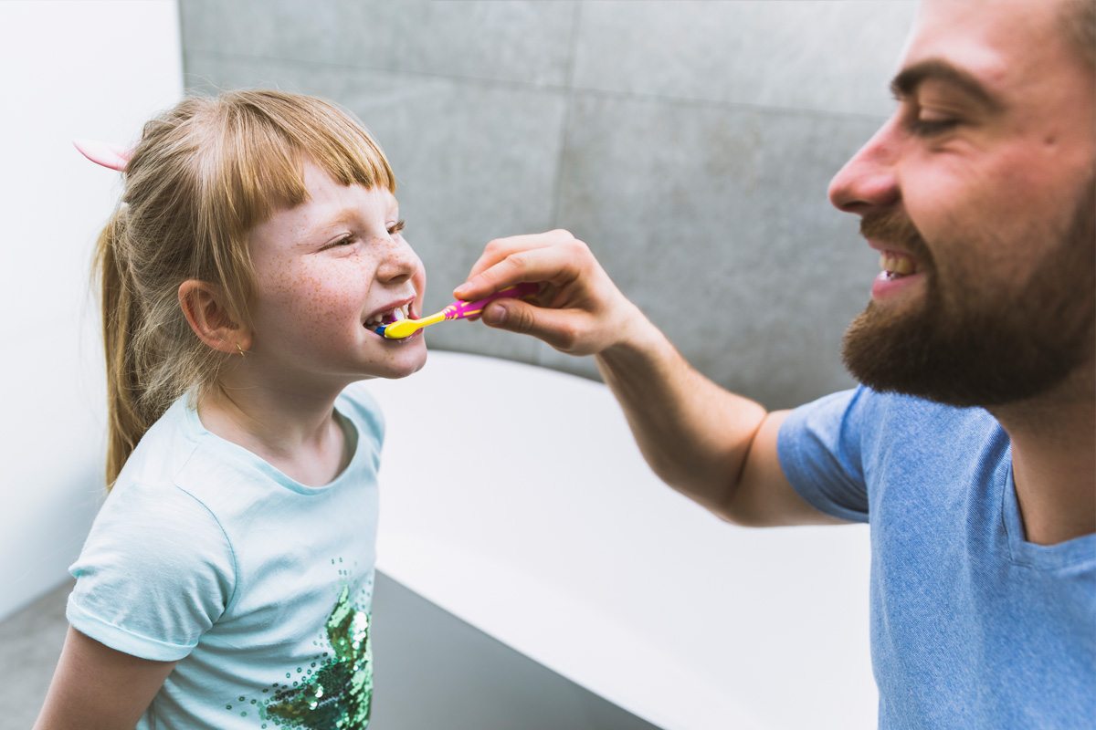Papà che lava i dentini alla figlia - insegnare la routine dell'igiene orale ai bambini