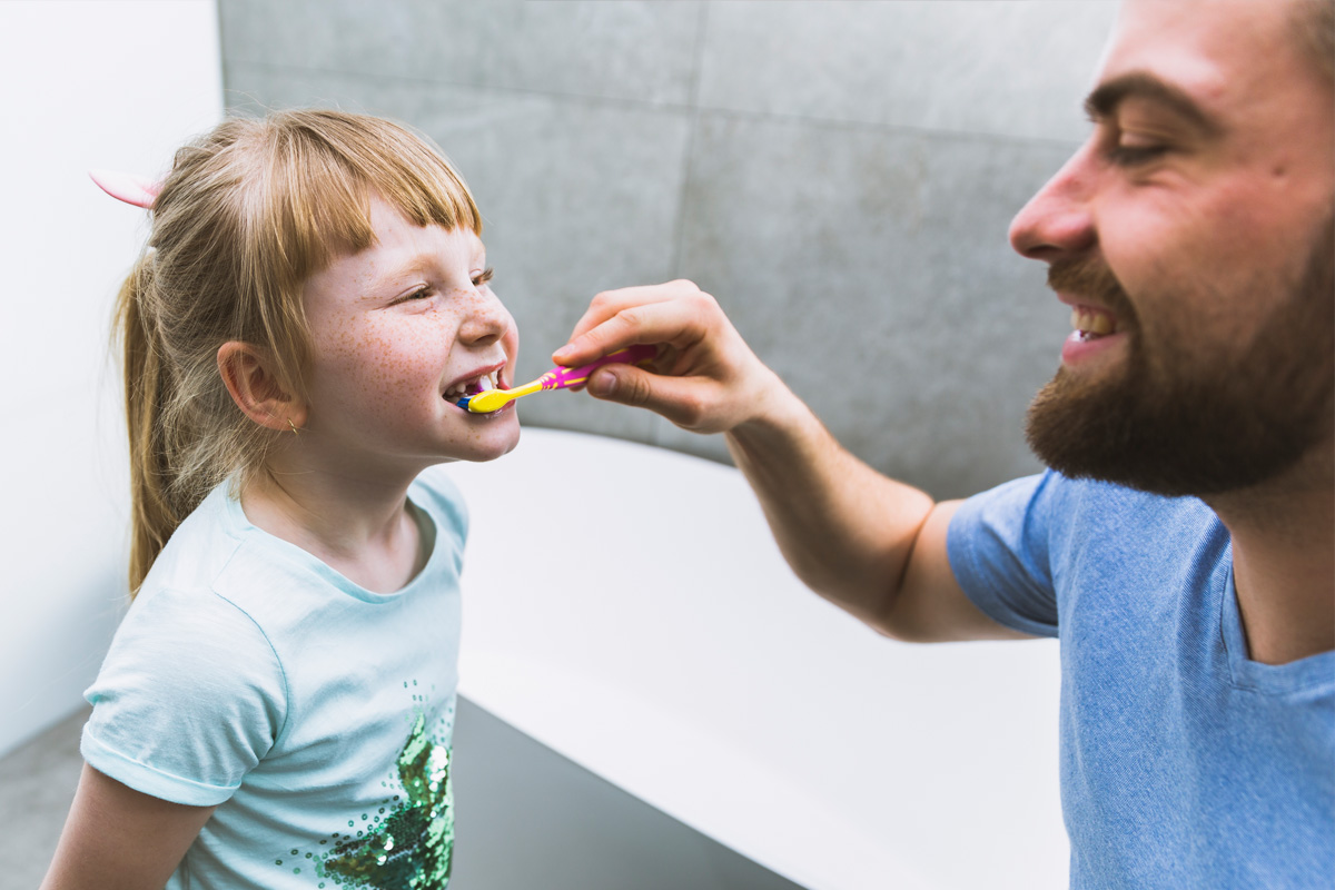 Pap che lava i dentini alla figlia - insegnare la routine dell'igiene orale ai bambini