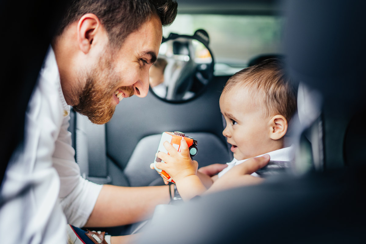 Papà che aggancia il suo bimbo sul seggiolino auto - sicurezza in auto