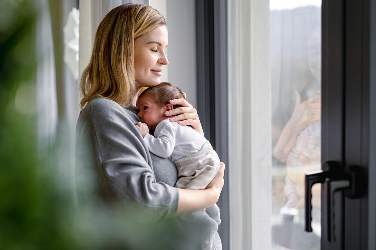 Mamma con neonato in braccio guarda dalla finestra